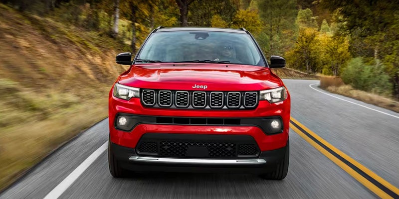 A red Jeep SUV driving on a winding road through a forested area