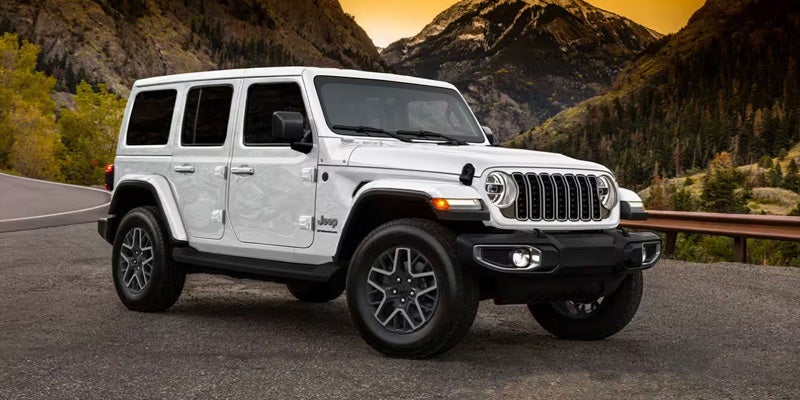 A white Jeep Wrangler parked on a paved overlook with tall mountains
