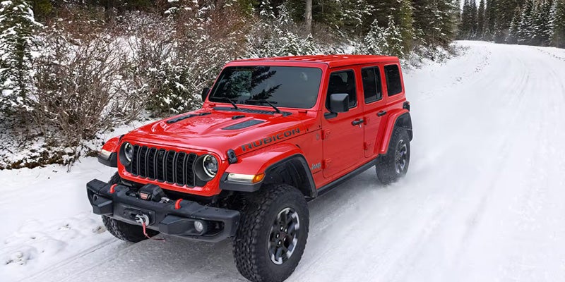 A red Jeep Wrangler driving along a snow-covered forest road