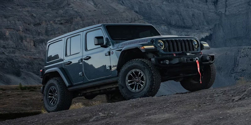 A dark-colored Jeep Wrangler climbing over rugged rocky terrain