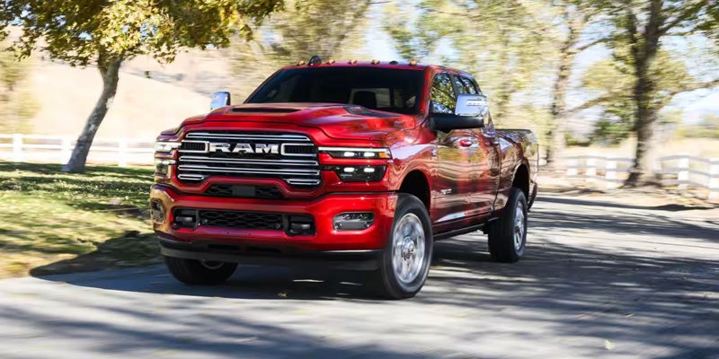 Red 2026 Ram 2500 Limited 4x4 driving on a sunny, tree-lined road, front three-quarters view.