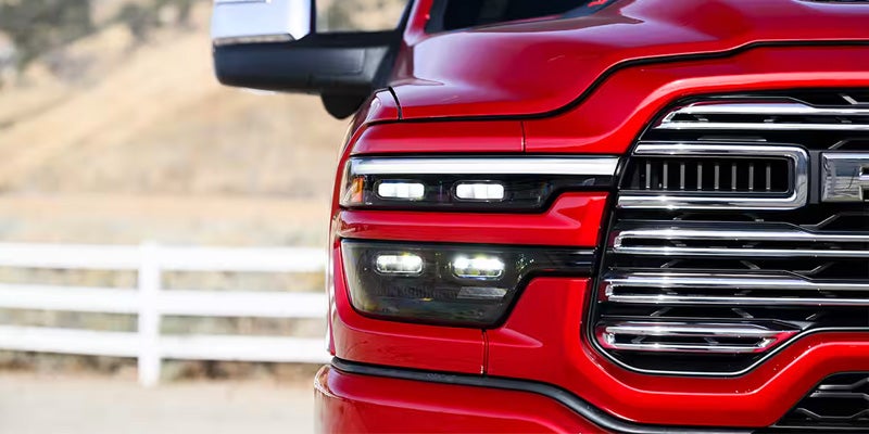 Close-up of the bright red front of a RAM pickup truck, showing its chrome grill and LED headlights.
