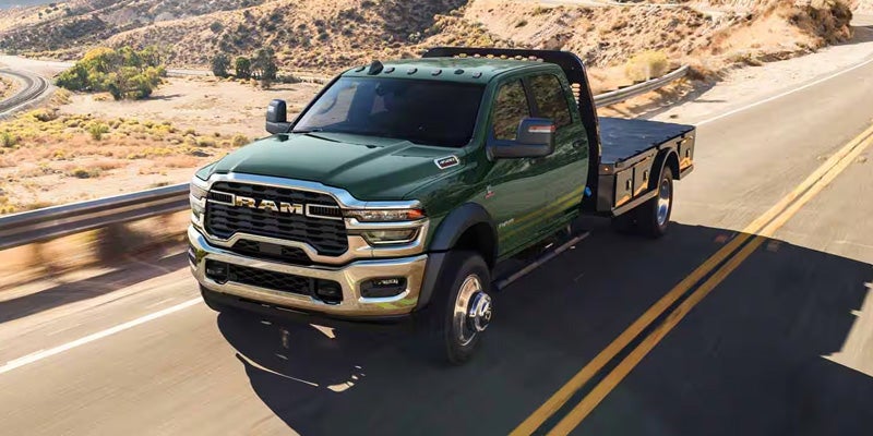 A green heavy-duty pickup truck with a flatbed driving on a highway through a sunlit